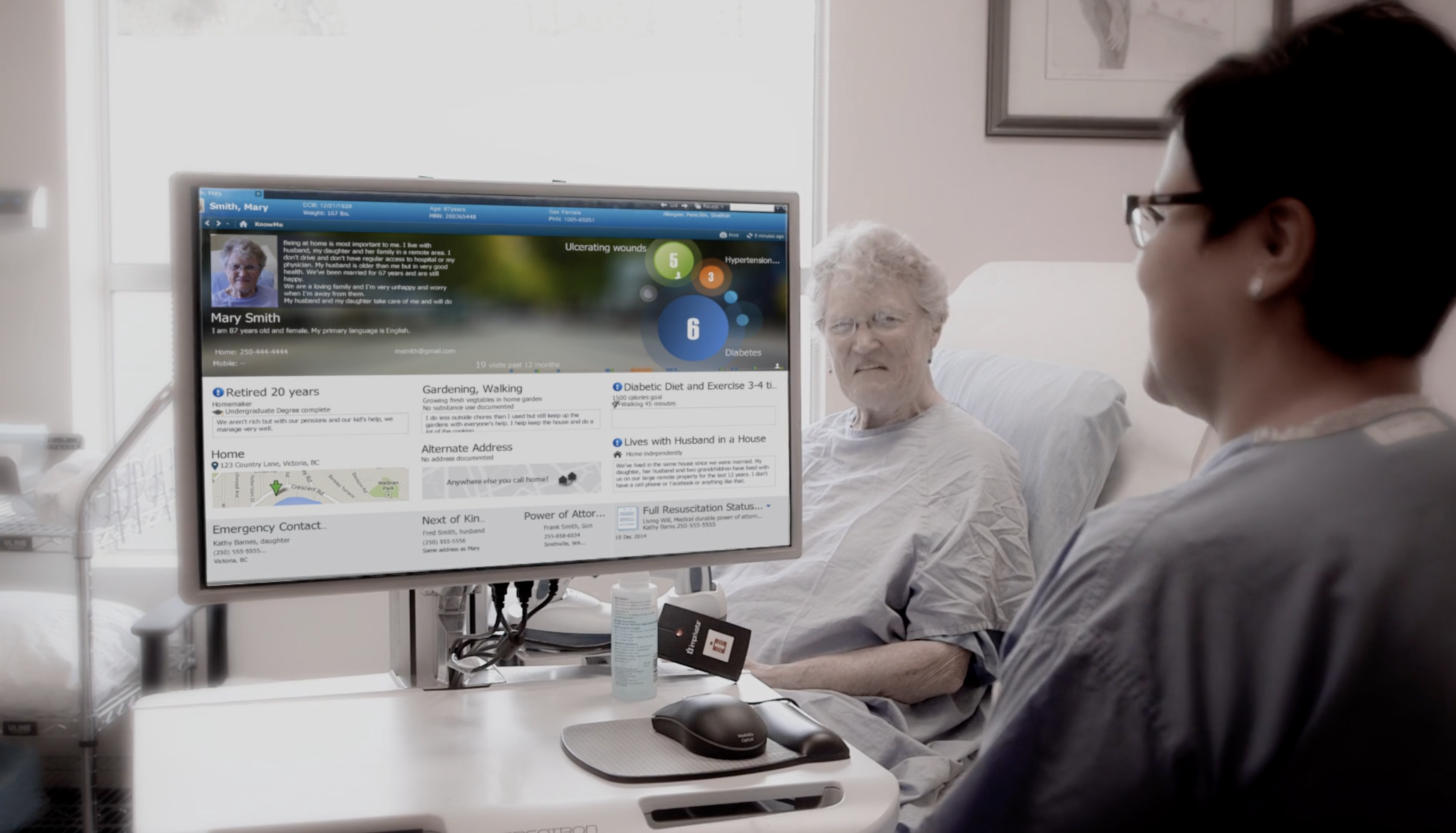 A clinician reviewing a patient's KnowMe profile on a bedside monitor with the patient